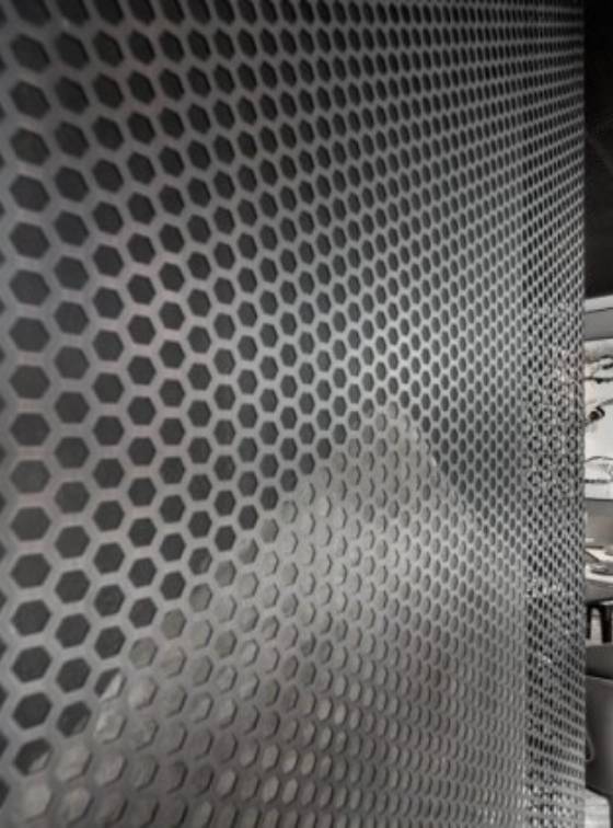 The room partition is made of hexagonal perforated metal.