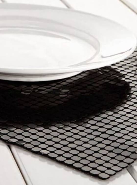 A black scale mesh curtain placemat is placed under a white dish.